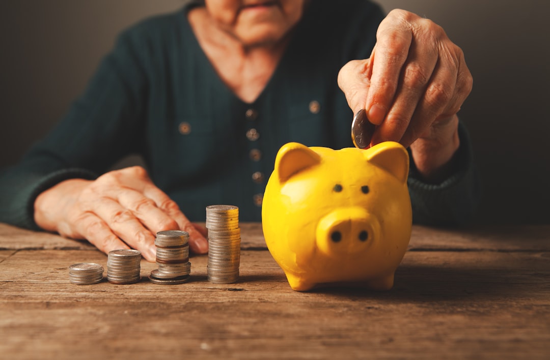 Elderly hands depositing coins into a yellow piggy bank.